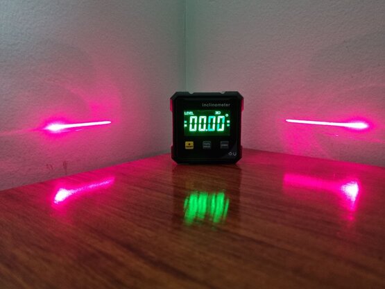An inclinometer showing a perfectly leveled surface, with lasers hitting the wall to the left and right